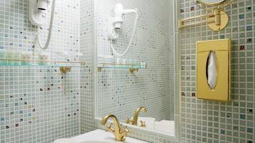 Un baño con lavamanos blanco, detalles dorados, un espejo y un perchero.