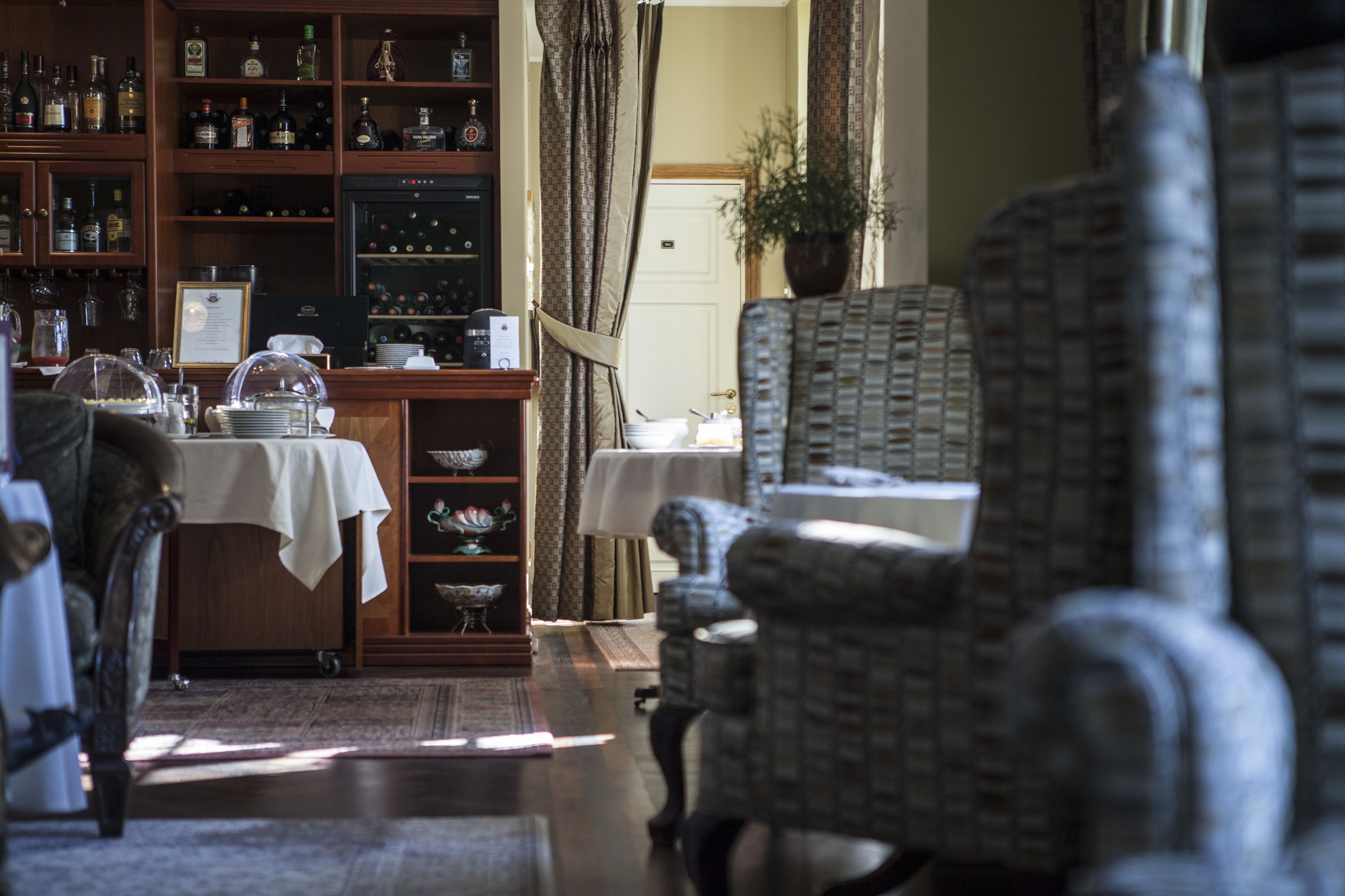 A room with a dining table, chairs, a bookshelf with various items, and a potted plant.
