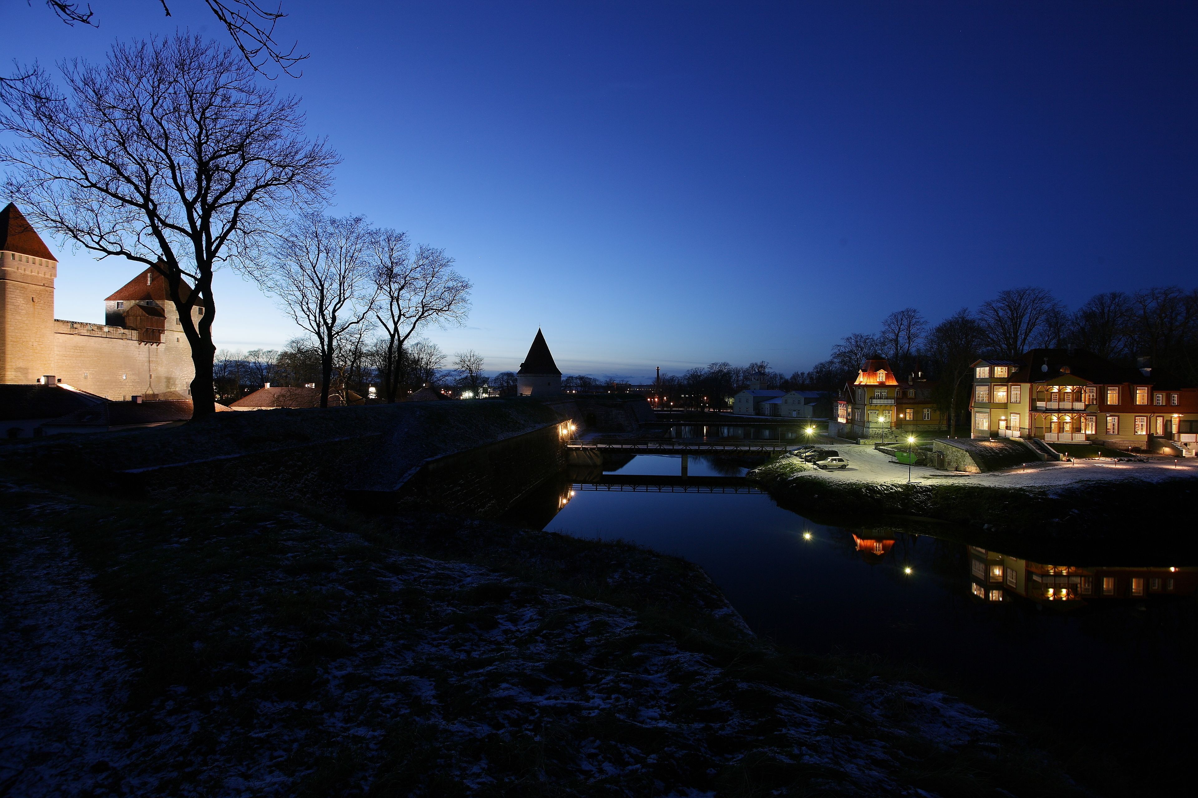 A historic building with a moat, a bridge, and a snow-covered landscape at dusk.