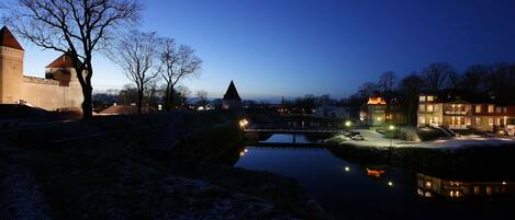 A historic building with a moat, a bridge, and a snow-covered landscape at dusk.