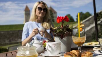 Una mesa dispuesta para una comida con tetera, tazas y pasteles, con vistas a un castillo al fondo.