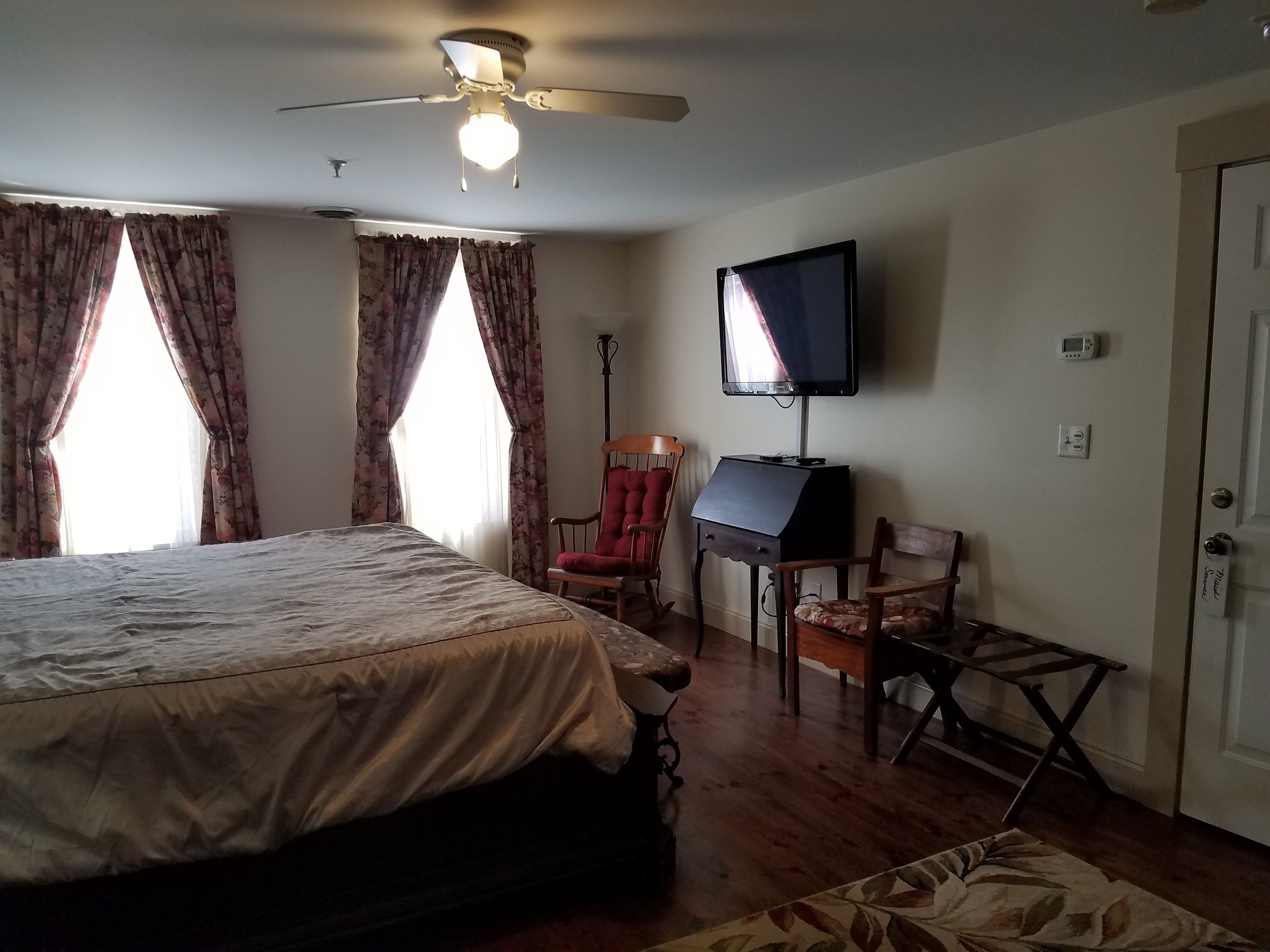 Un dormitorio con cama, escritorio, silla, televisión y ventilador de techo.