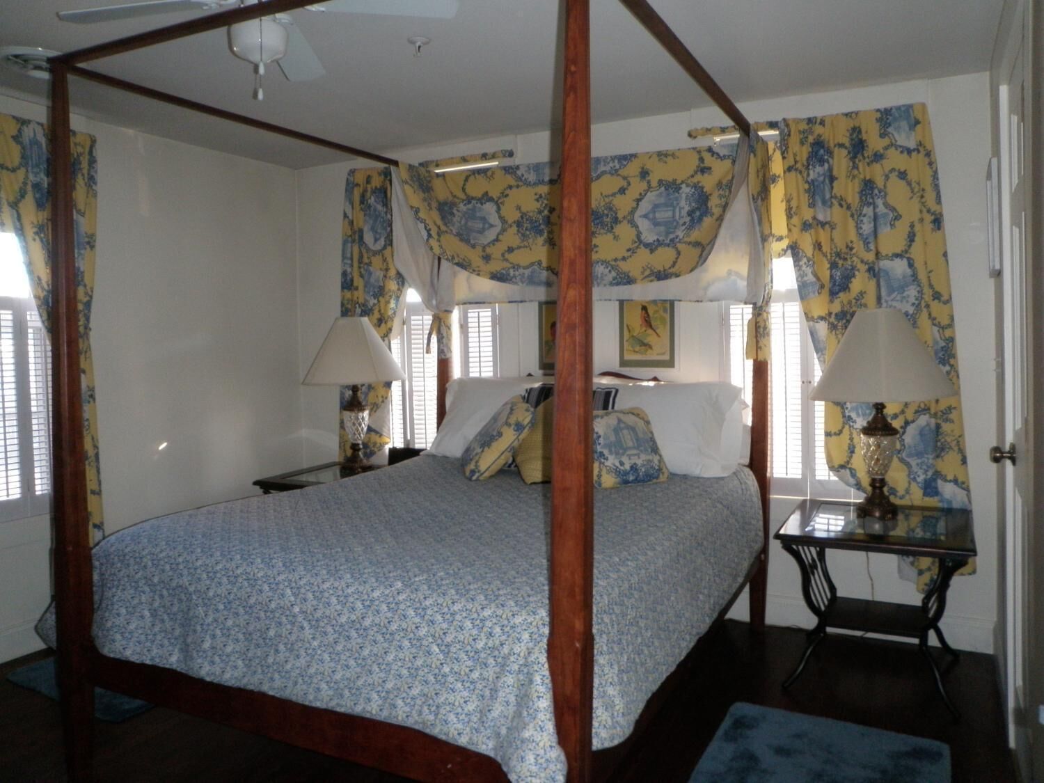 A four-poster bed with a floral bedspread, two bedside lamps, and a nightstand with a lamp.