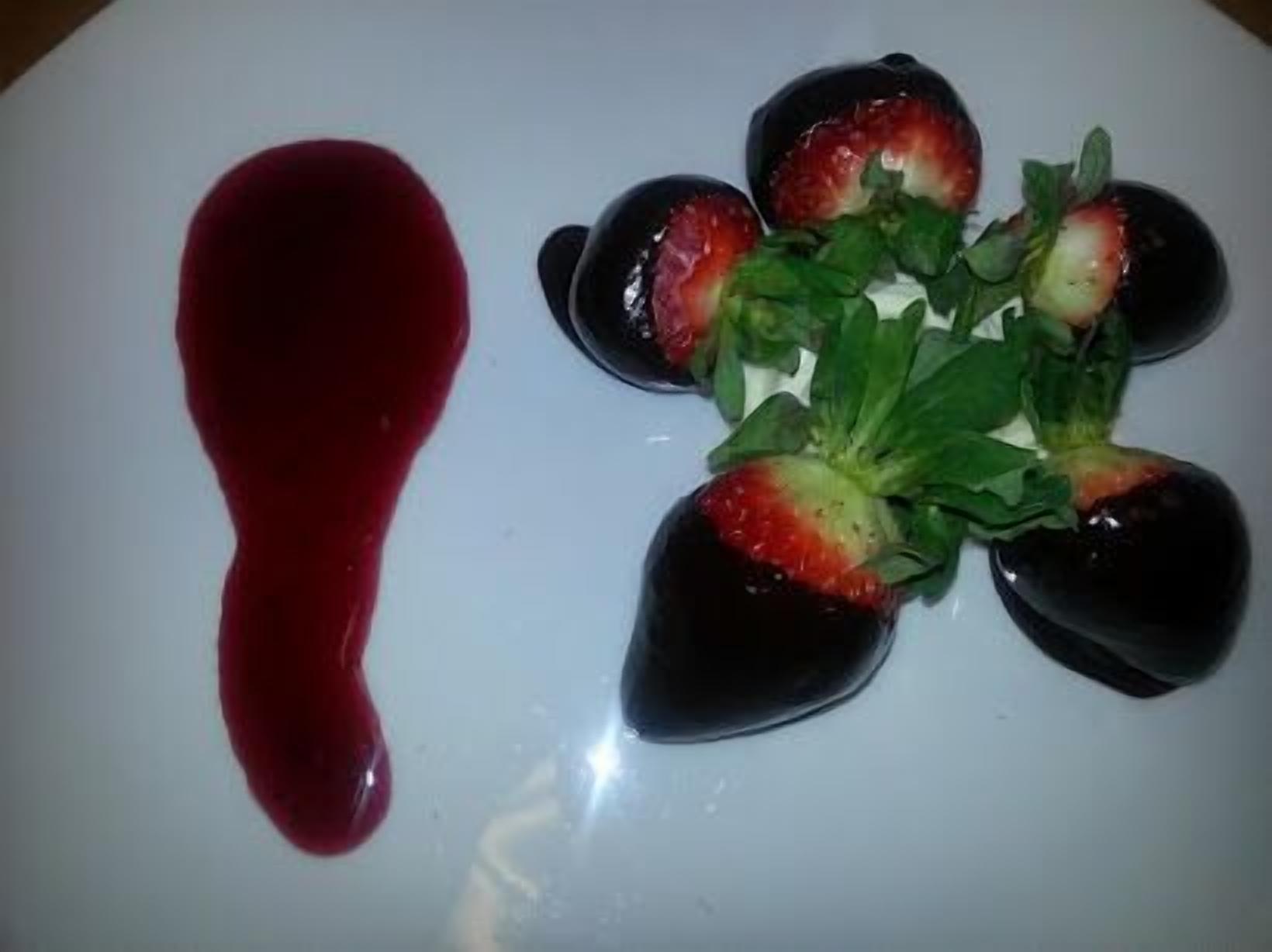 Un plato blanco con cuatro fresas y una cucharada de salsa roja.