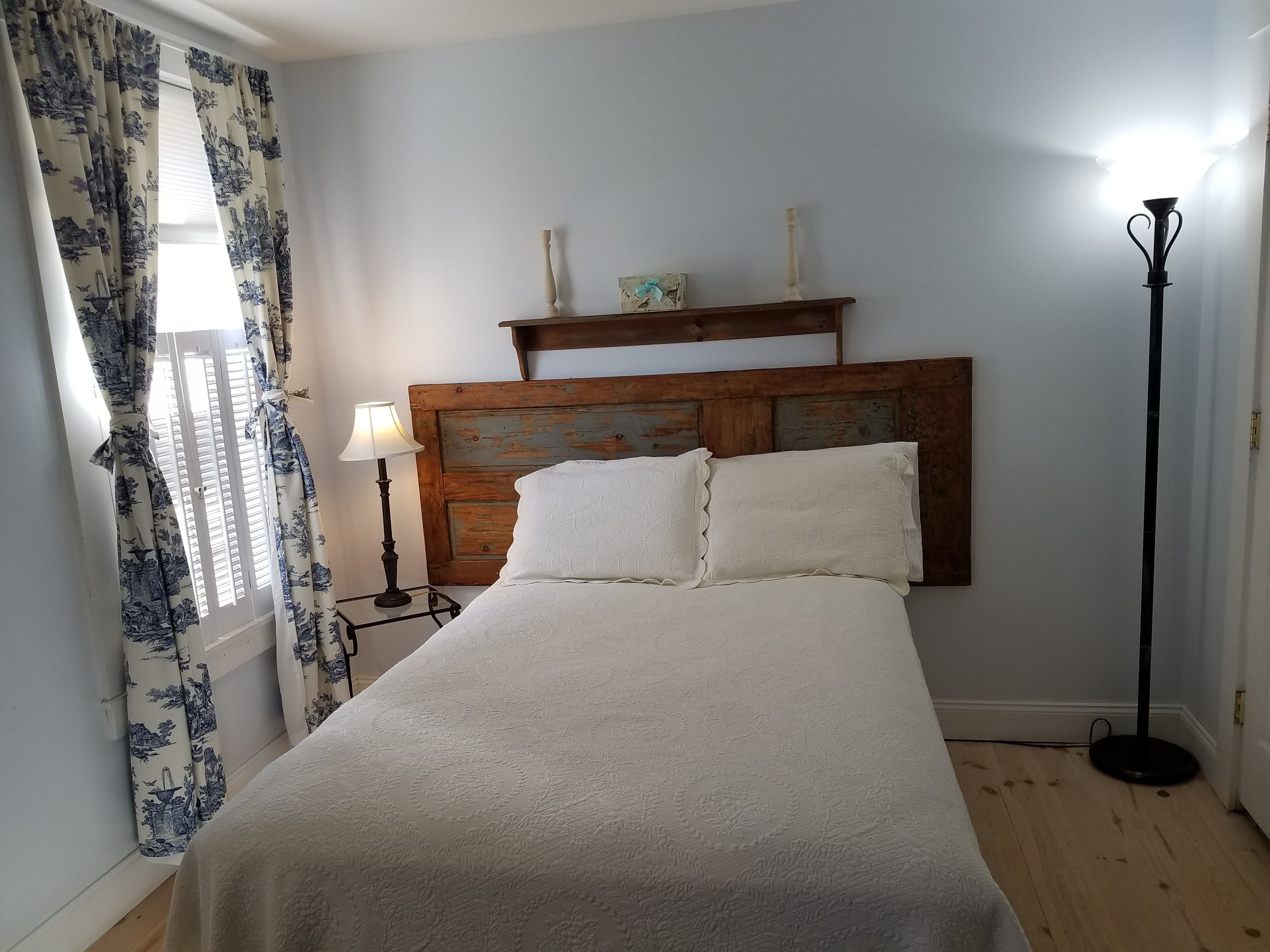 A bedroom with a wooden headboard, a bed with white bedding, a nightstand with a lamp, and a floor lamp.