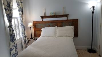 A bedroom with a wooden headboard, a bed with white bedding, a nightstand with a lamp, and a floor lamp.