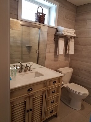 Une salle de bain avec un meuble-lavabo en bois, un évier, des toilettes et une fenêtre agrémentée d’un pot à fleurs.