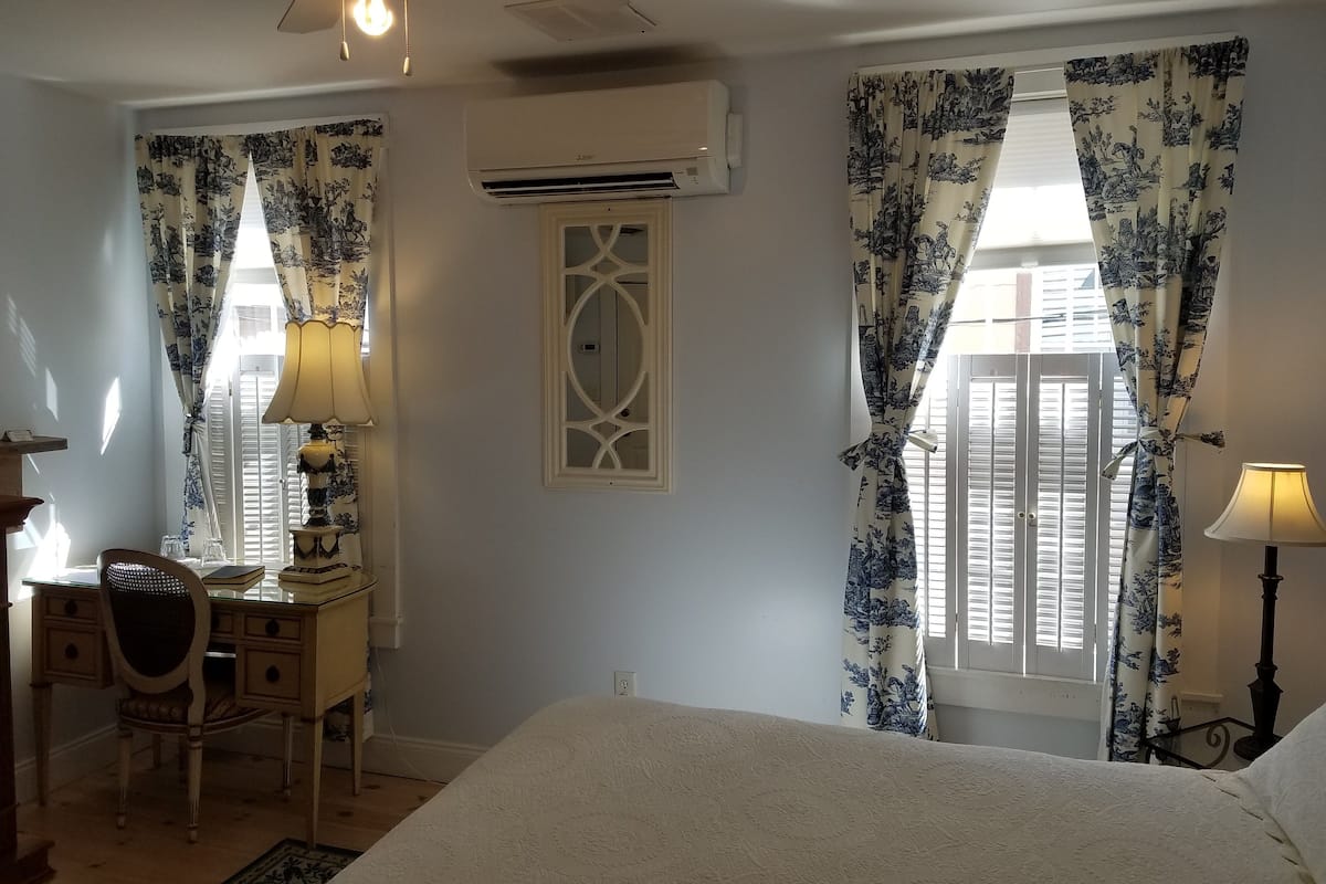 Un dormitorio con una cama, un escritorio con silla, dos lámparas y un ventilador de techo.