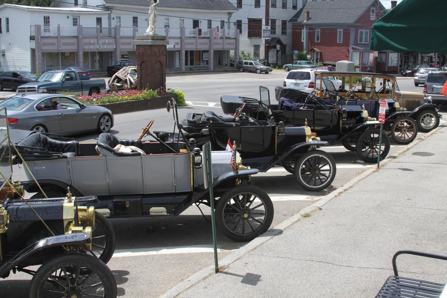 A row of vintage cars parked in a lot with buildings in the background.