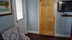 A room with a sliding wooden door, a mounted flat-screen TV, a patterned armchair, and a framed picture on the wall. - Tilton Inn (Tilton)