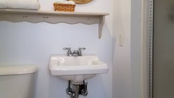 Une salle de bain avec des toilettes, un lavabo et un miroir. On y trouve des serviettes et un panier sur une étagère au-dessus du lavabo.