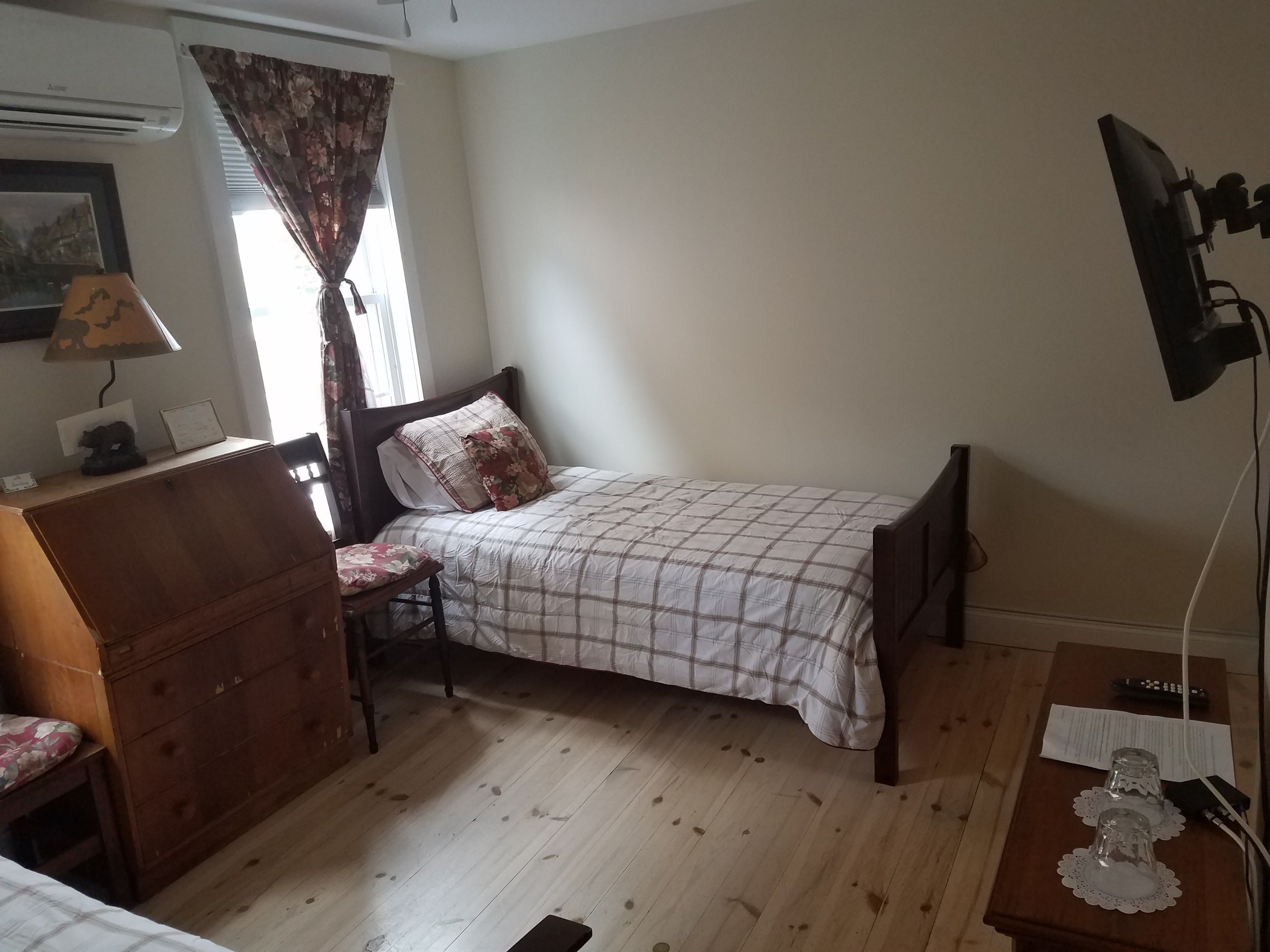 Un dormitorio con una cama individual, un aparador de madera, una silla, un escritorio con lámpara y un televisor.