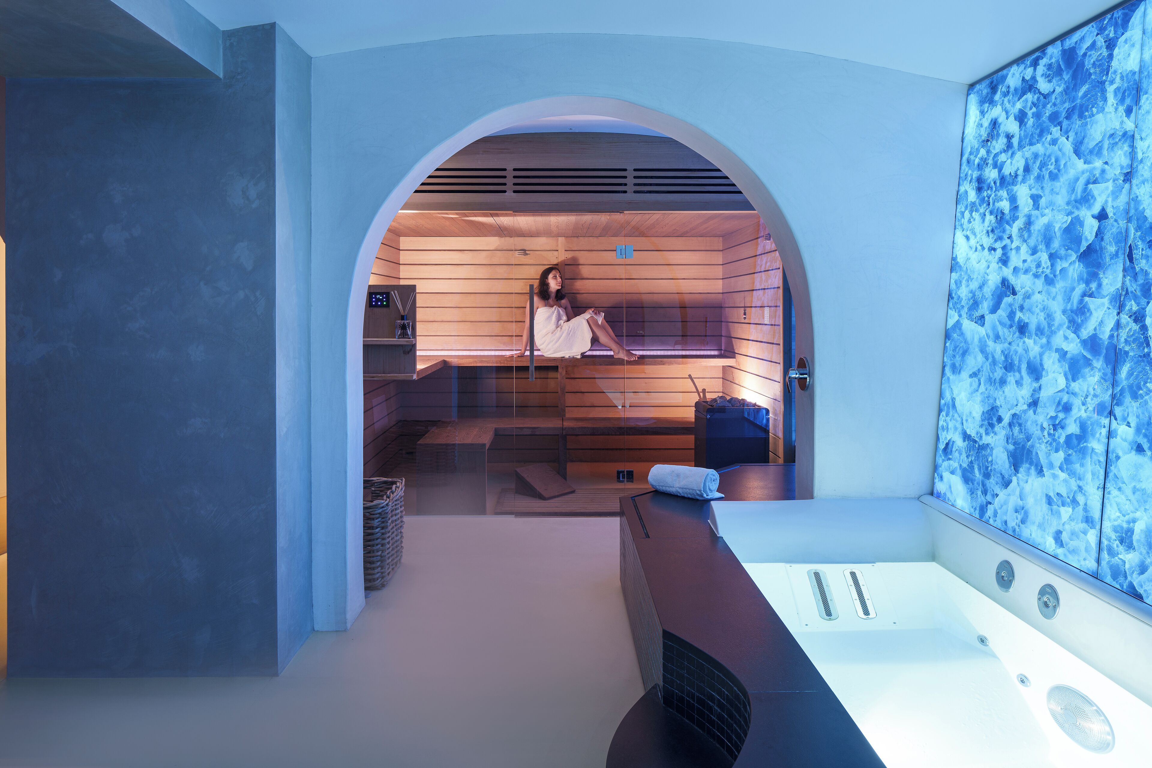 A modern spa room with a wooden sauna, a large bathtub, and a wall-mounted massage table.