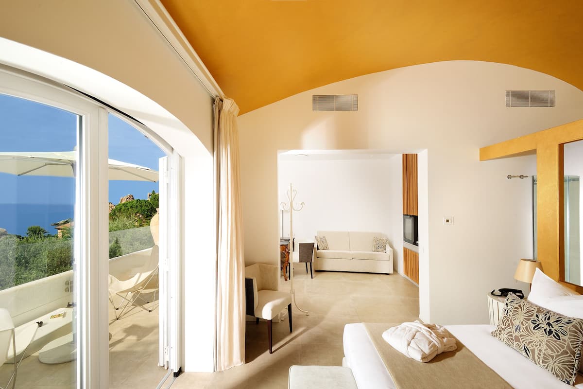 A modern hotel room with a balcony, a sofa, a TV, and a dining area.
