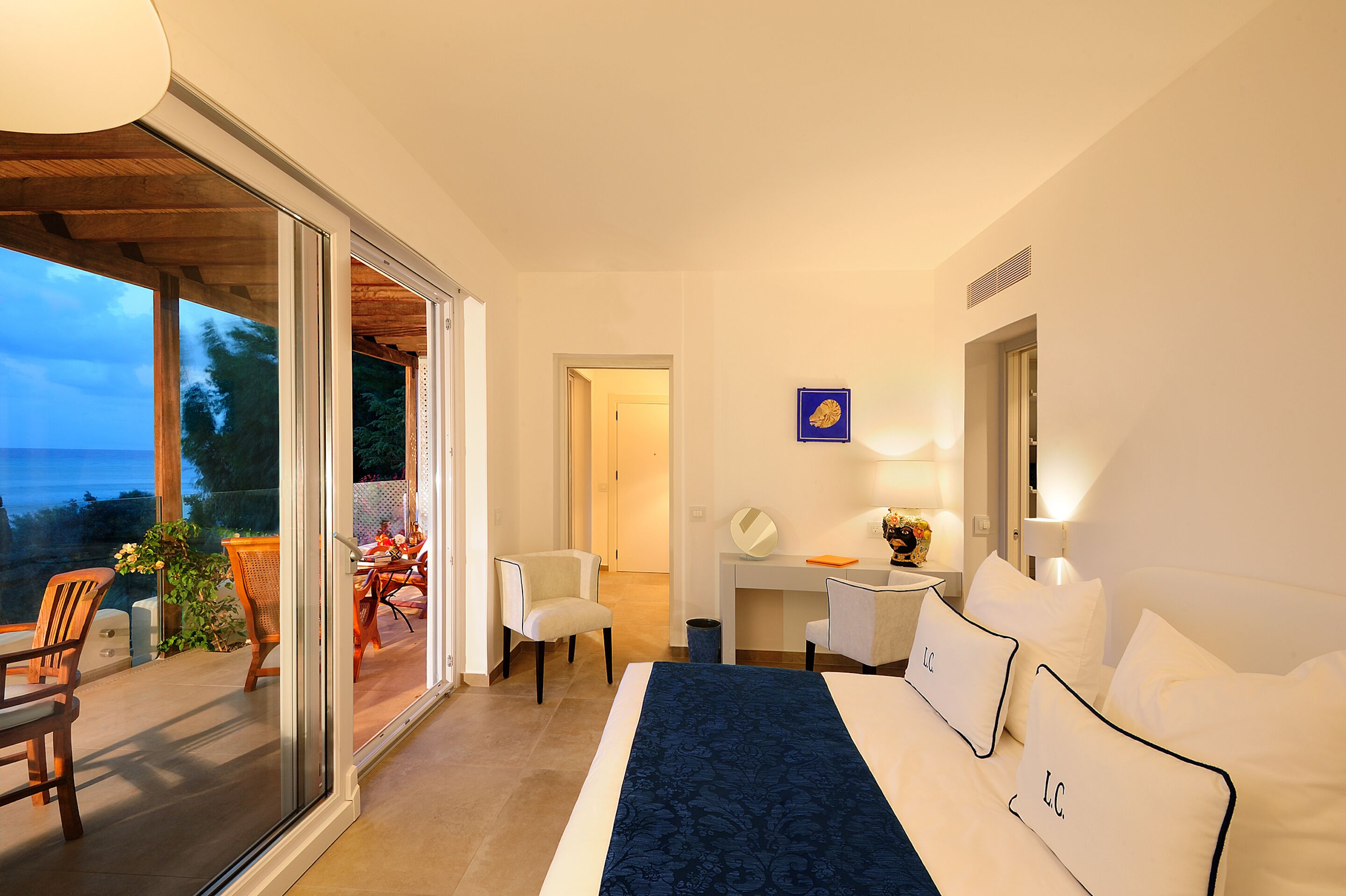 Une chambre d’hôtel avec un lit, un bureau et une vue sur un espace extérieur aménagé avec des chaises et une table, accessible par une porte coulissante.