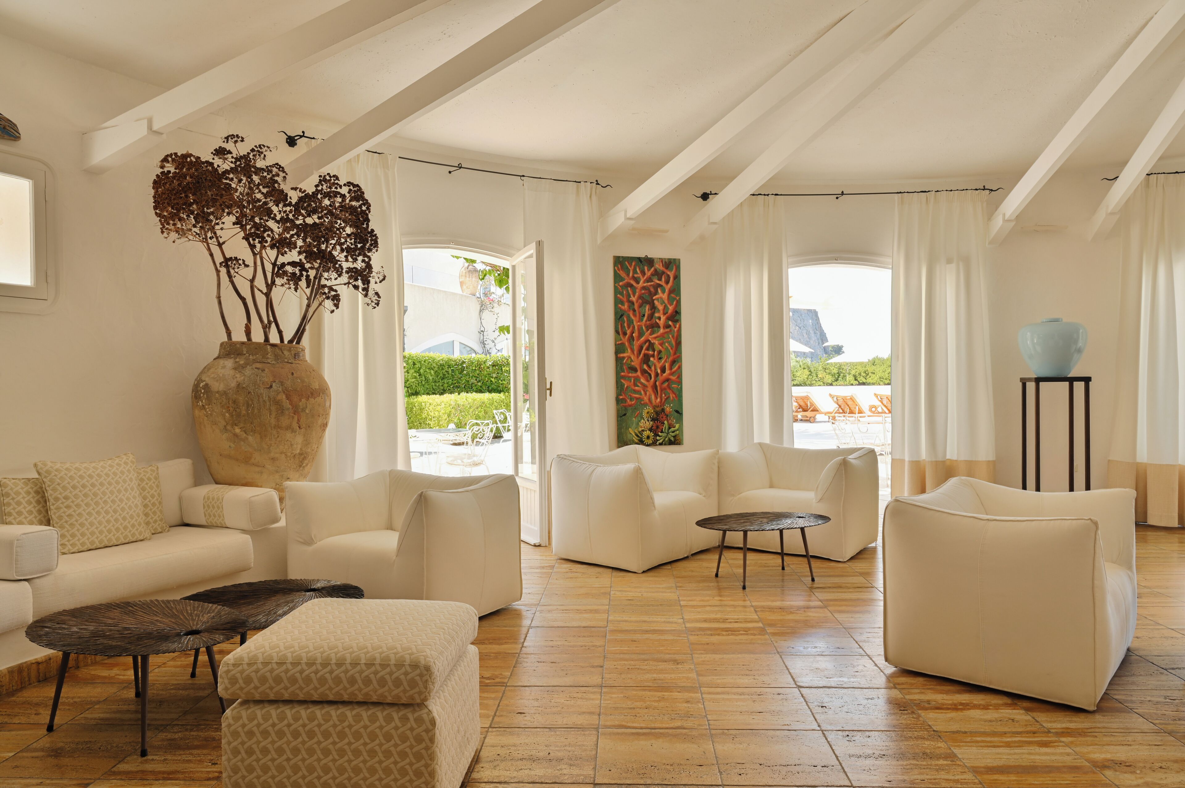 Amplia sala de estar con sofás blancos, un jarrón grande con plantas y vistas al exterior.