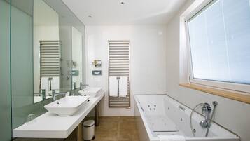 A modern bathroom with a large mirror, two sinks, a bathtub, and a window.