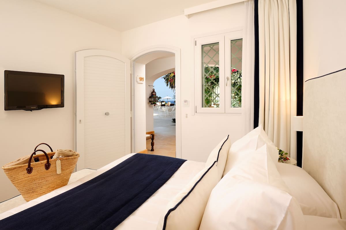 A hotel room with a bed, a television, a wicker basket, and a view of the outdoor area.