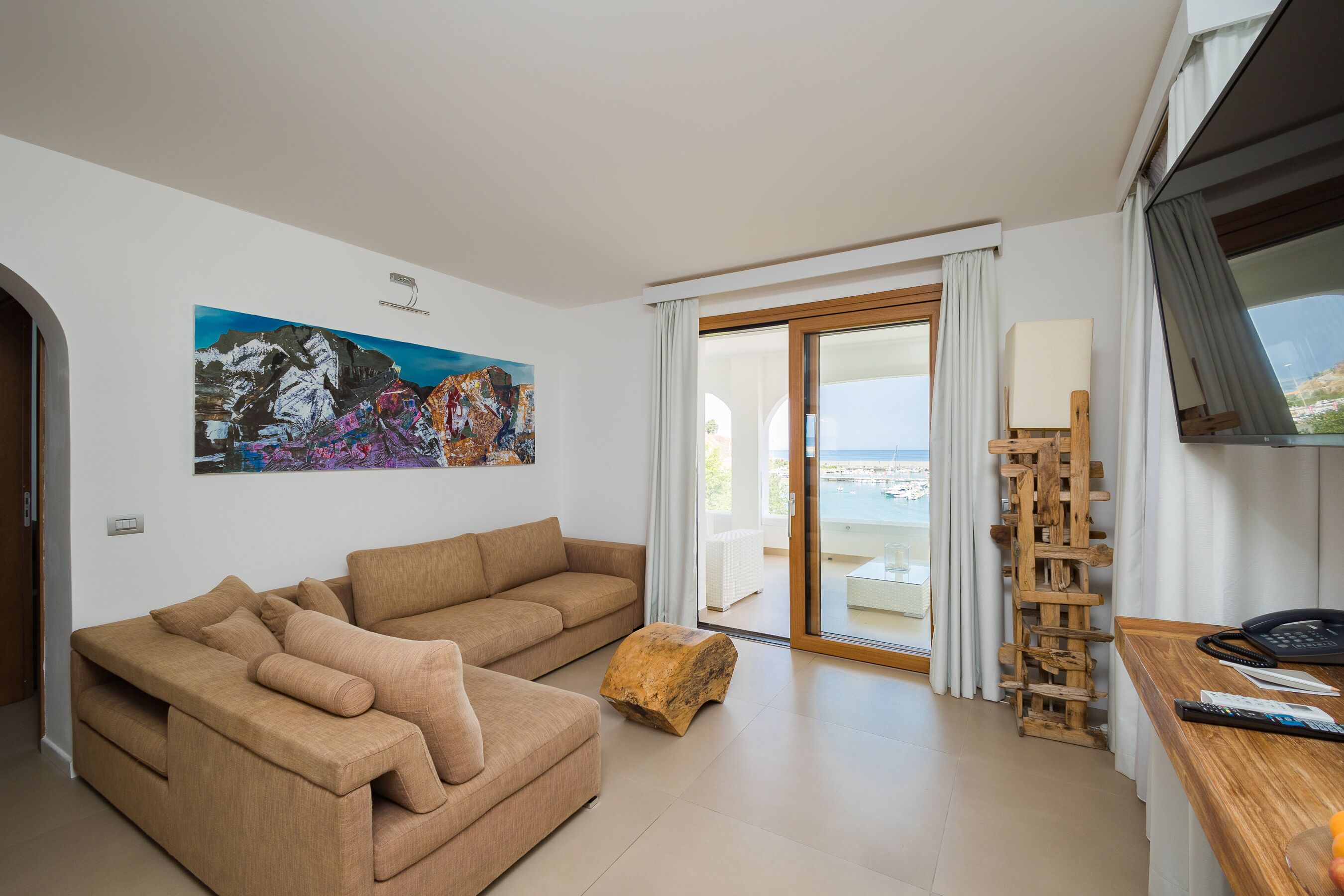 A modern living room with a beige sofa, a wooden coffee table, and a painting of mountains.