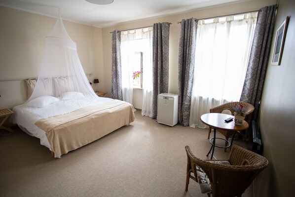 A hotel room with a bed, a small table, a chair, and a window with curtains. - Kuursaal Guesthouse (Kuressaare)