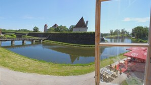 A view of a castle and a moat from a window overlooking a patio area with outdoor seating.