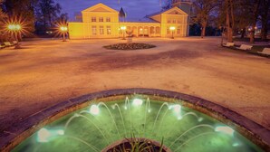 A large building with a symmetrical facade, a central fountain, and a well-maintained lawn with benches.