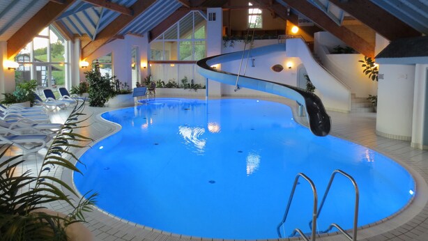 An indoor swimming pool with a sloped ceiling and a slide. - Hotel Stockhausen GbR (Schmallenberg)