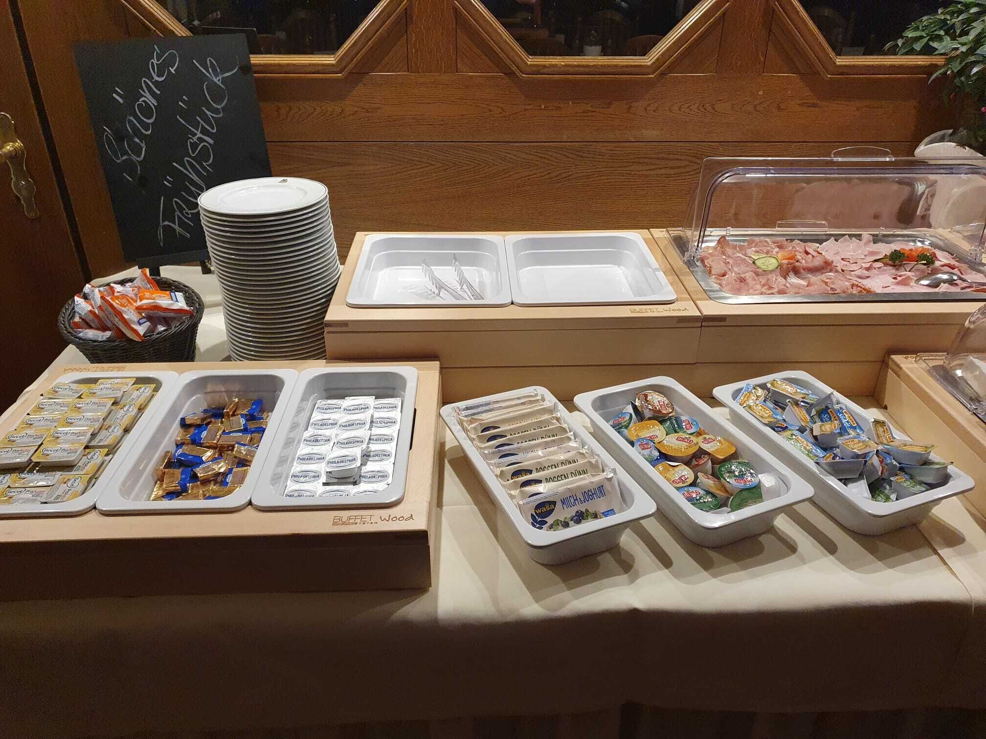 Montaje de bufé con bandejas de comida, incluyendo carnes y quesos, y un letrero que dice 'Buffet Wood'.