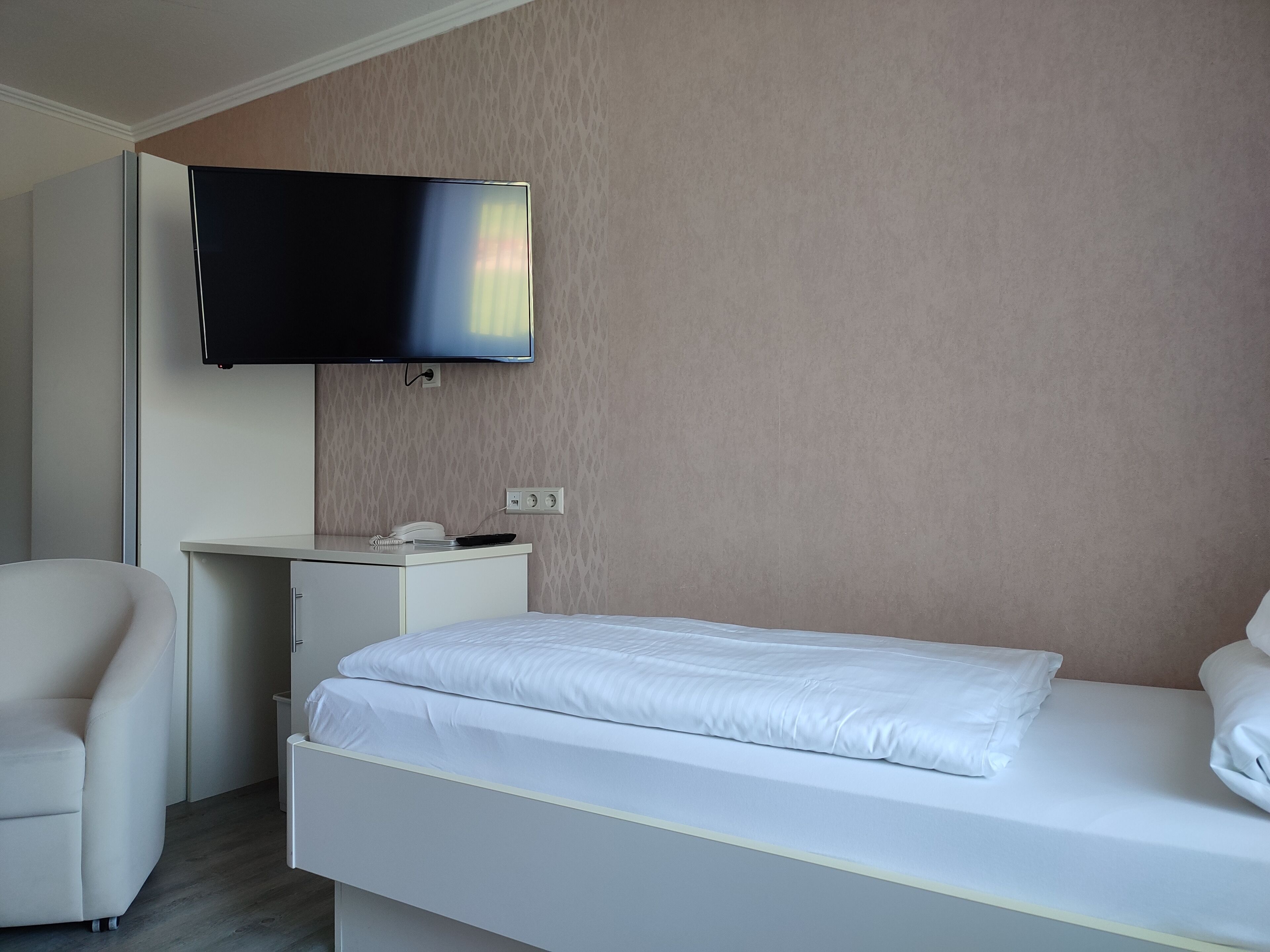 Una habitación de hotel moderna con una cama, un escritorio y un televisor instalado en la pared.