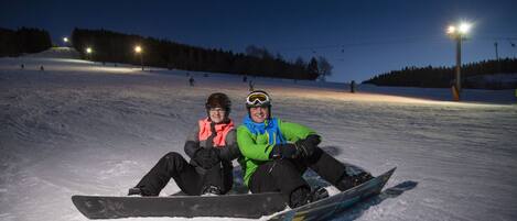 Pendiente nevada con una persona sentada sobre una tabla de snowboard.