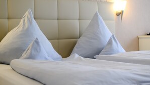 A neatly made bed with white linens and pillows, a tufted headboard, and a wall-mounted light fixture. - Hotel Stockhausen GbR (Schmallenberg)