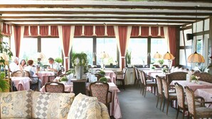 A restaurant with multiple tables and chairs, covered with pink tablecloths. There are potted plants and hanging lamps. - Hotel Stockhausen GbR (Schmallenberg)