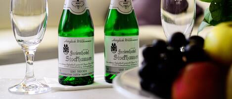 Two green bottles of Sekt Trocken next to three clear glasses on a table, with a bowl of grapes and a bouquet of flowers in the background.