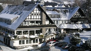 A traditional chalet-style building with multiple stories, large windows, and a sloped roof covered in snow. - Hotel Stockhausen GbR (Schmallenberg)