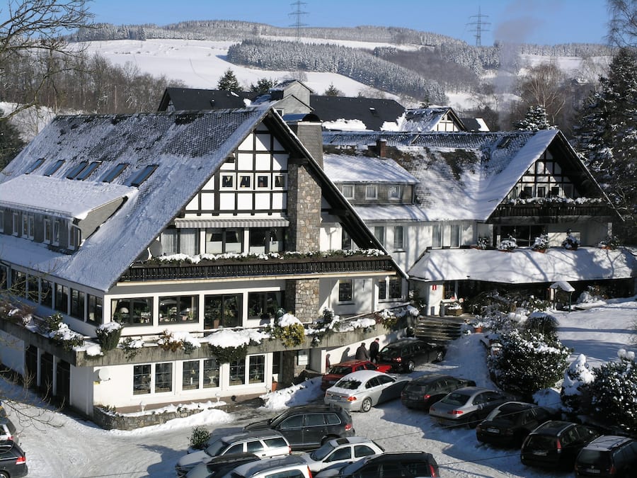 A traditional chalet-style building with multiple stories, large windows, and a sloped roof covered in snow.