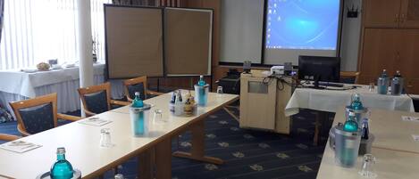 A conference room with tables, chairs, and a projector screen.