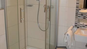 Ducha con cerramiento de vidrio, cabezal de ducha de mano y llave en la pared.