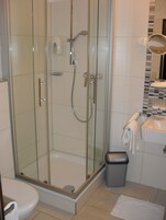 Ducha con cerramiento de vidrio, cabezal de ducha de mano y llave en la pared.