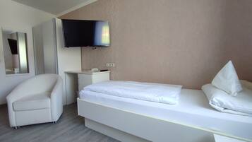 Una habitación de hotel con cama, una silla, un escritorio, un televisor de pantalla plana y un espejo.