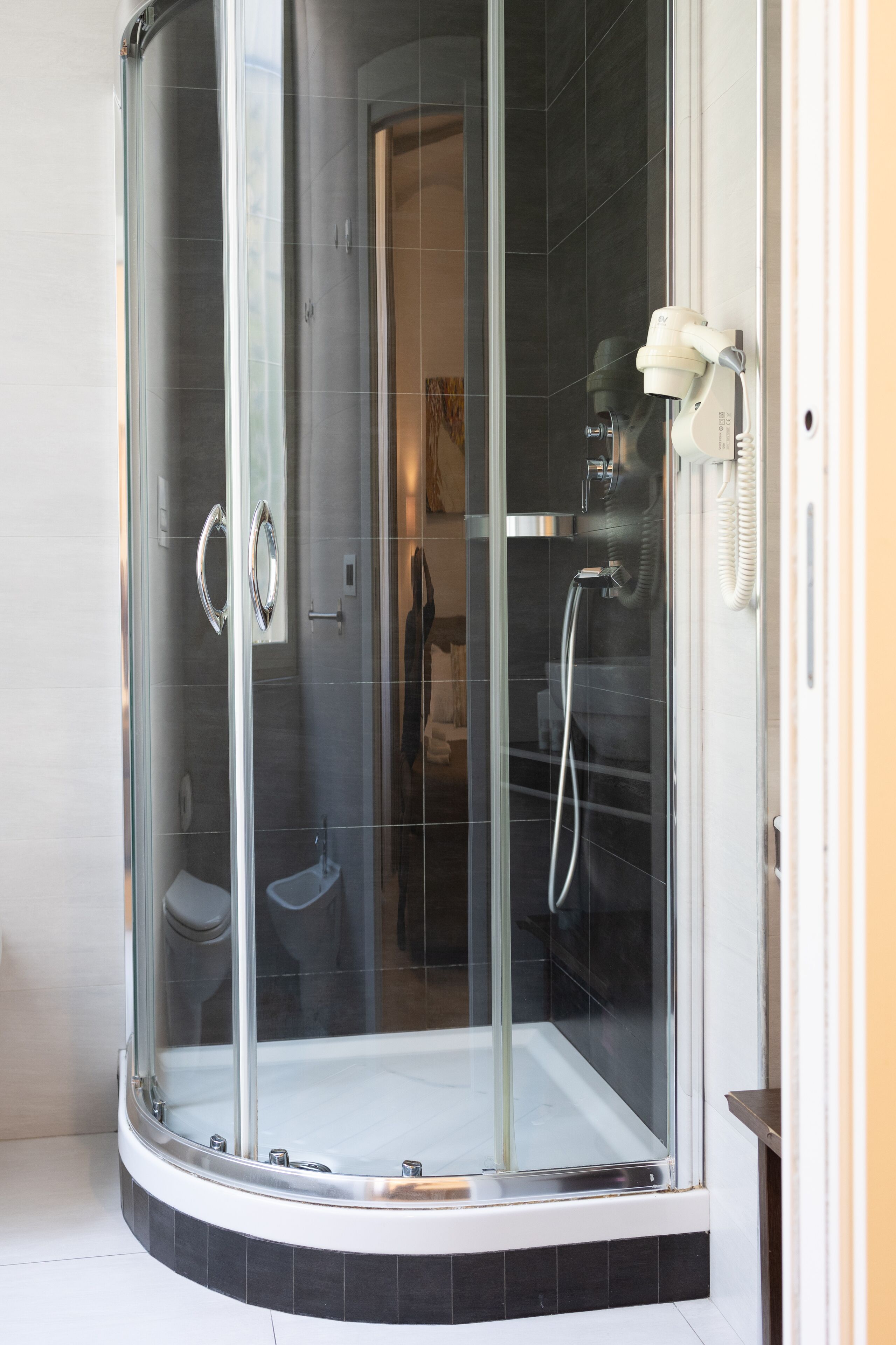 Eine Duschkabine mit Glaswänden, einer Handbrause und einem am Wand montierten Wasserhahn.