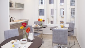 A modern dining area with two round tables, grey upholstered chairs, and a view of the city through large windows. - Maison Maneli Luxury B&B (Rome)