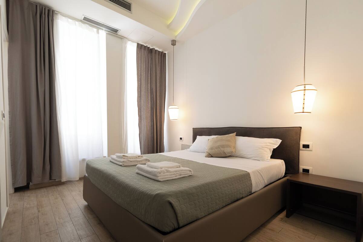 A modern hotel room with a large bed, a bedside table, and a nightstand.