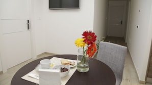 A modern room with a round table, a flat-screen TV mounted on the wall, and a vase with flowers. - Maison Maneli Luxury B&B (Rome)