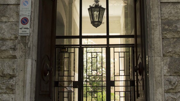 A building entrance with a decorative archway, a metal gate, and a hanging lantern. - Maison Maneli Luxury B&B (Rome)