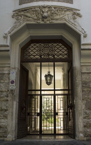 A building entrance with a decorative archway, a metal gate, and a hanging lantern. - Maison Maneli Luxury B&B (Rome)