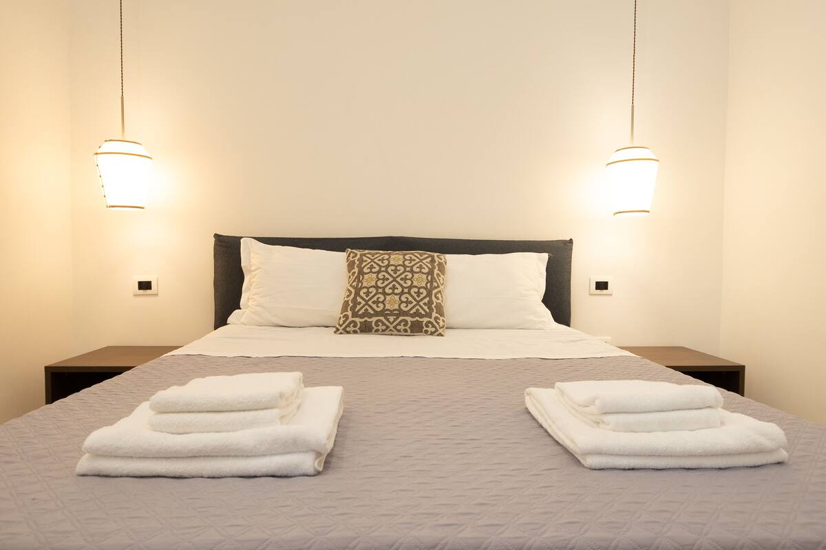 A neatly made bed with a patterned pillow, two bedside tables, and two wall-mounted lights.
