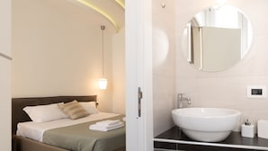 A hotel room with a bed, a large round mirror, a white sink, and a wall socket. - Maison Maneli Luxury B&B (Rome)