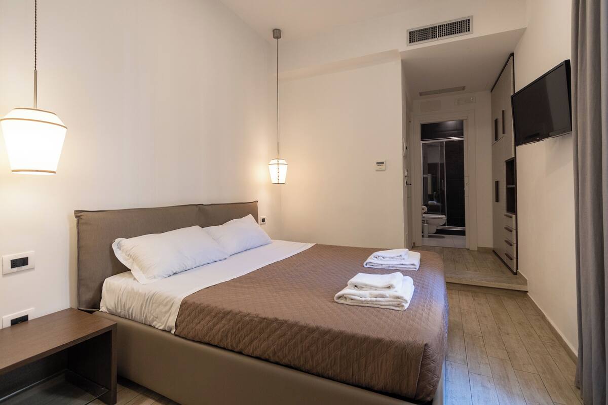 A hotel room with a bed, bedside table, and a TV mounted on the wall.