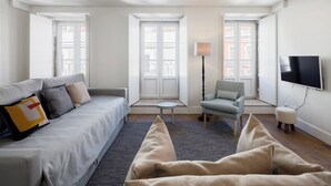 A modern living room with a sofa, armchair, and a TV mounted on the wall. - LSA Bairro Alto by Numa (Lisbon)