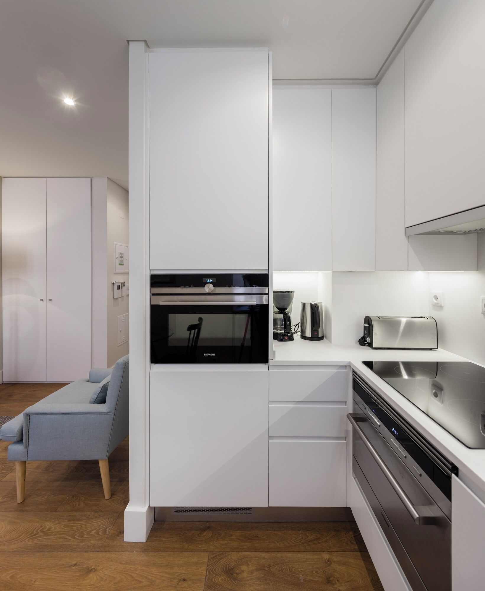 A modern kitchen with white cabinetry, a built-in oven, a coffee machine, and a dishwasher.